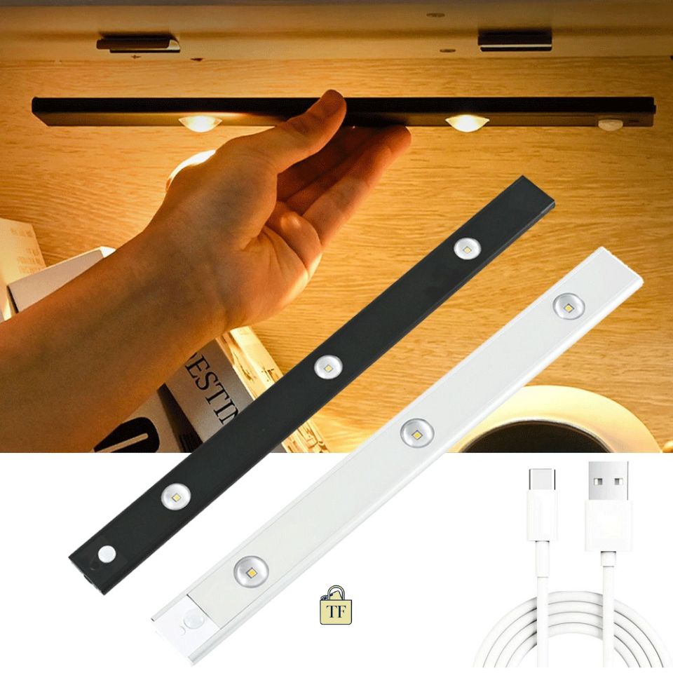 Hand holding a black LED strip light above a wooden surface with additional strips and a USB cable displayed below.